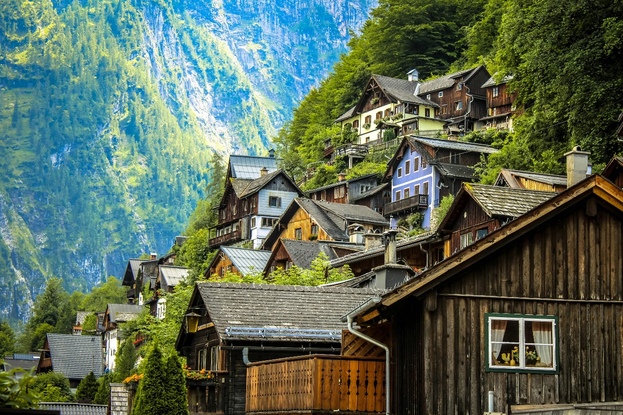 Picturesque Austrian Alpine village with traditional wooden houses nestled against dramatic mountain cliffs, showcasing Austria's stunning natural beauty and charming architecture that complements its excellence in arts and music education