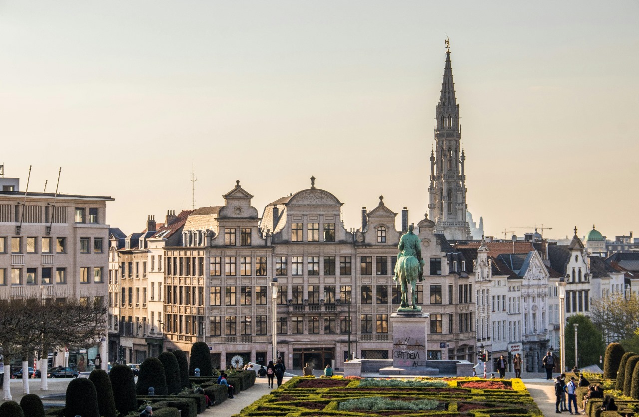 Brussels with the iconic Town Hall spire, historic guild houses with ornate facades, bronze equestrian statue, and formal gardens, showcasing Belgium's position as Europe's heart with rich architectural heritage and strong international programs
