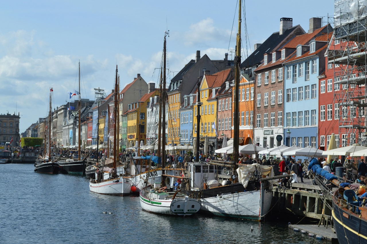 Copenhagen's famous Nyhavn district with colorful 17th-century townhouses lining the canal and historic sailing ships, representing Denmark's design excellence and sustainable innovation