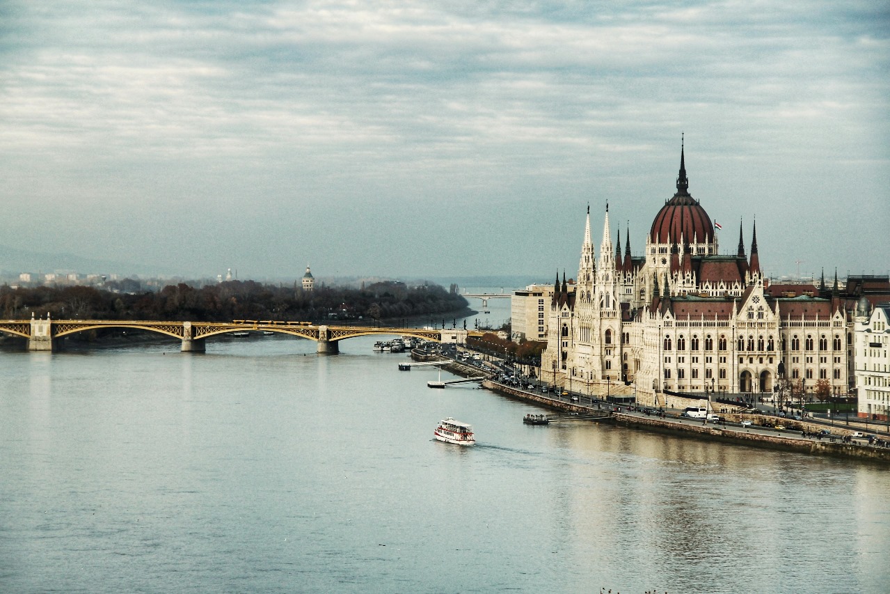 Stunning panoramic view of Budapest's Hungarian Parliament Building with its distinctive red dome along the Danube River, with the historic Chain Bridge visible, representing Hungary's architectural grandeur and affordable medical education