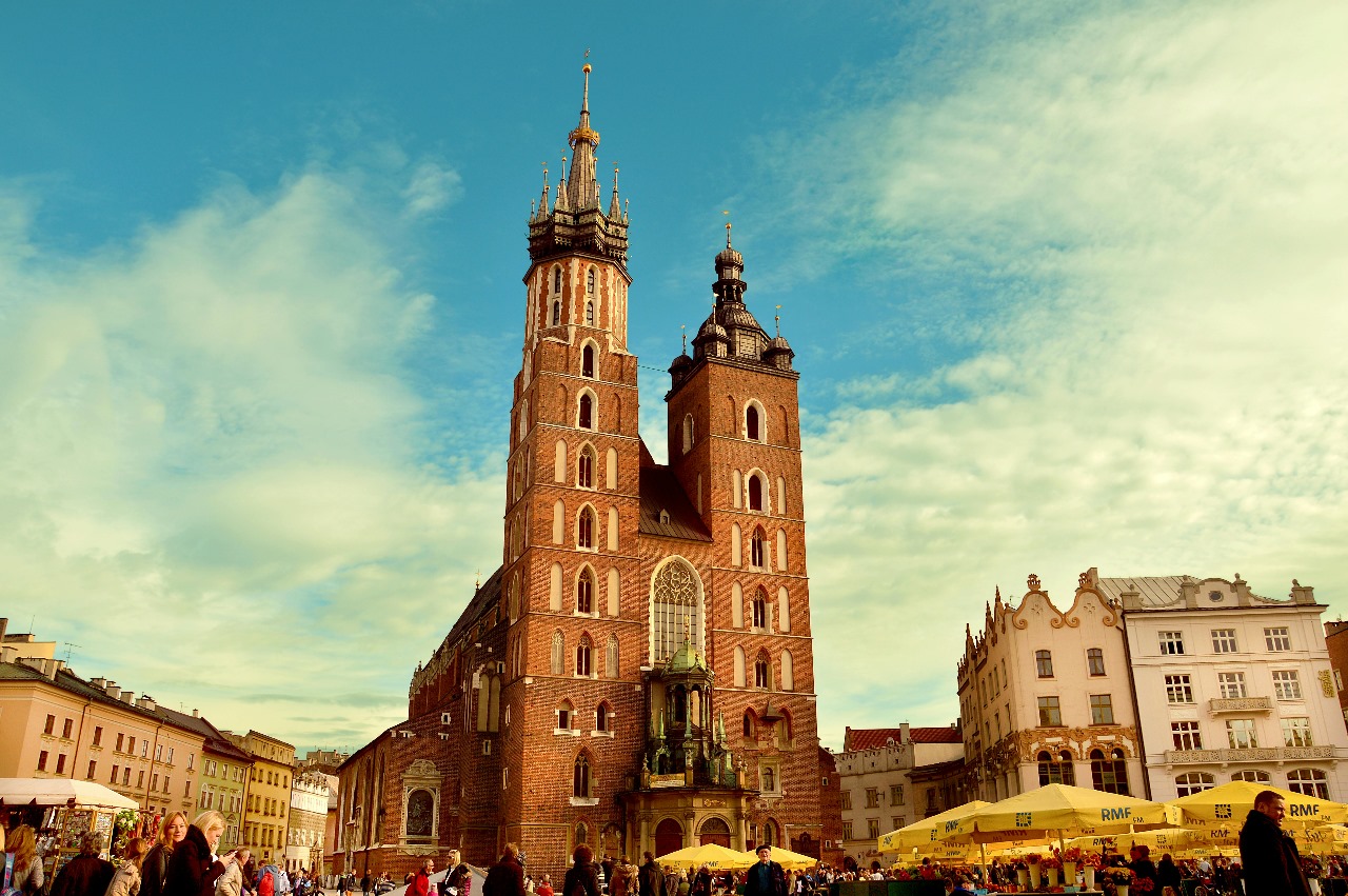 Krakow's Main Market Square featuring the iconic St. Mary's Basilica with twin towers, surrounded by historic buildings and outdoor cafes, showcasing Poland's medieval charm and growing education reputation
