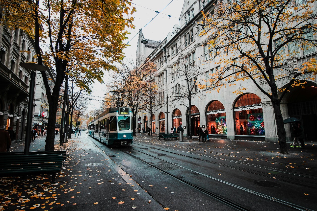 Charming Swiss city street with modern tram on cobblestone roads, autumn foliage, and historic architecture, representing Switzerland's blend of tradition and innovation in education